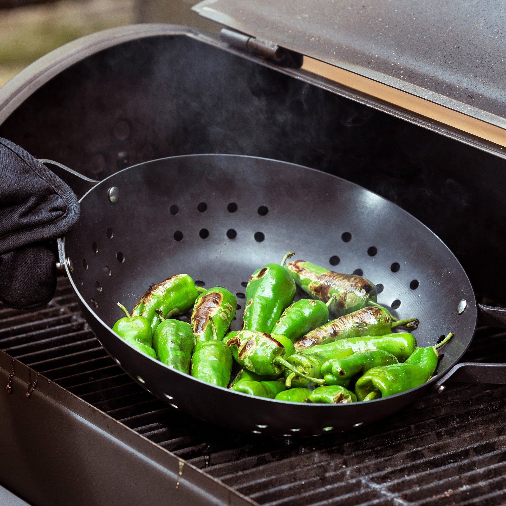 Merten & Storck Carbon Steel BBQ Wok 30cm zwart met groene peppers op de BBQ