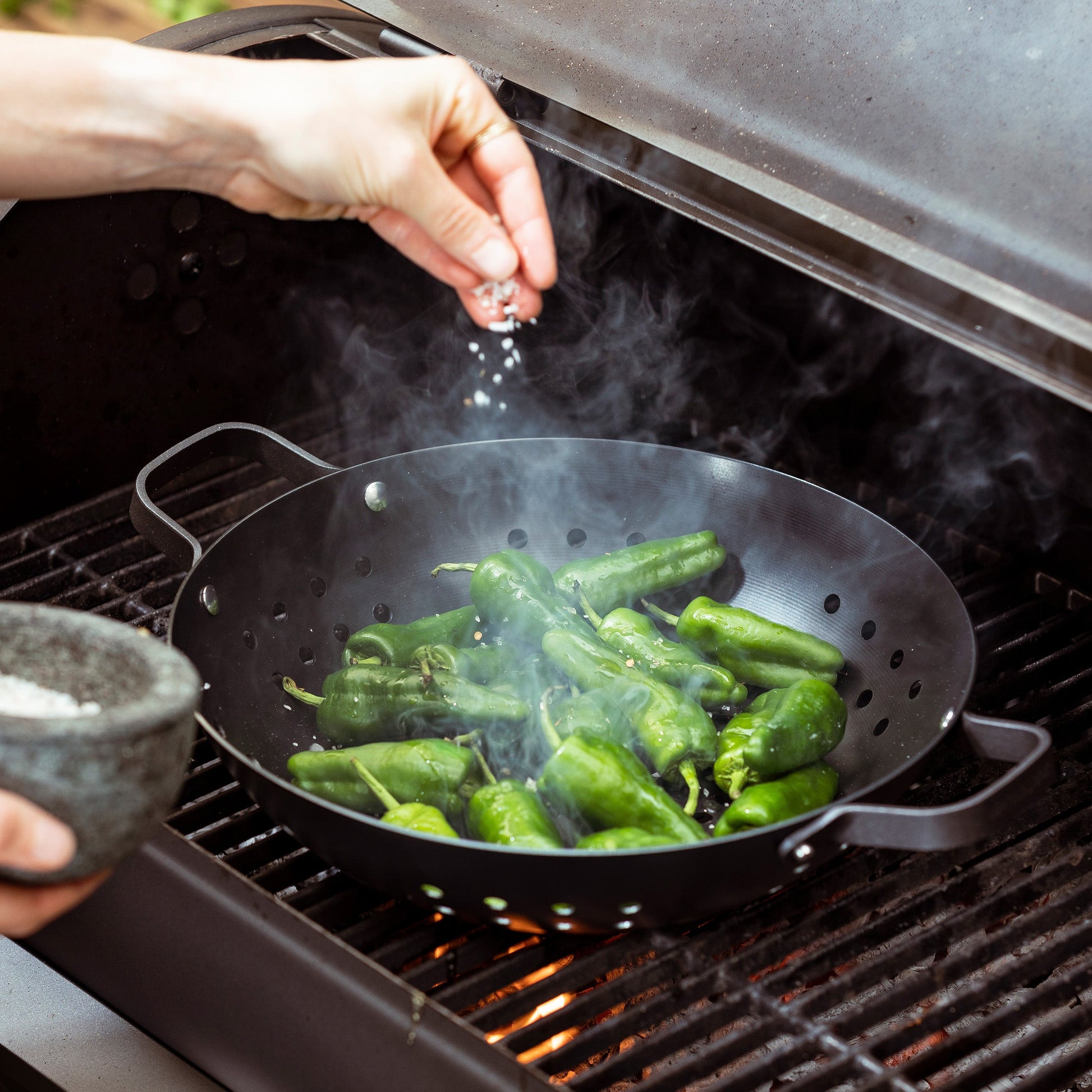 Merten & Storck Carbon Steel BBQ Wok 30cm zwart met groene peppers op de BBQ